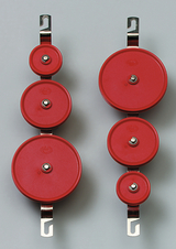 Das Bild zeigt eine Anordnung von roten Rollen mit unterschiedlichen Durchmessern, die an metallischen Halterungen befestigt sind. Diese Teile sind wahrscheinlich für physikalische Experimente im Bildungsbereich gedacht, um Konzepte wie Mechanik und Kräfte zu veranschaulichen.