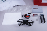 Das Bild zeigt eine Reihe von Laborutensilien, darunter Messbecher, Schutzbrille, Kabel und eine Batterie, die für chemische Experimente im Bildungsbereich verwendet werden können. Zusätzlich sind eine Anleitung und ein Experimentiergerät sichtbar, die die Durchführung von Versuchen unterstützen.