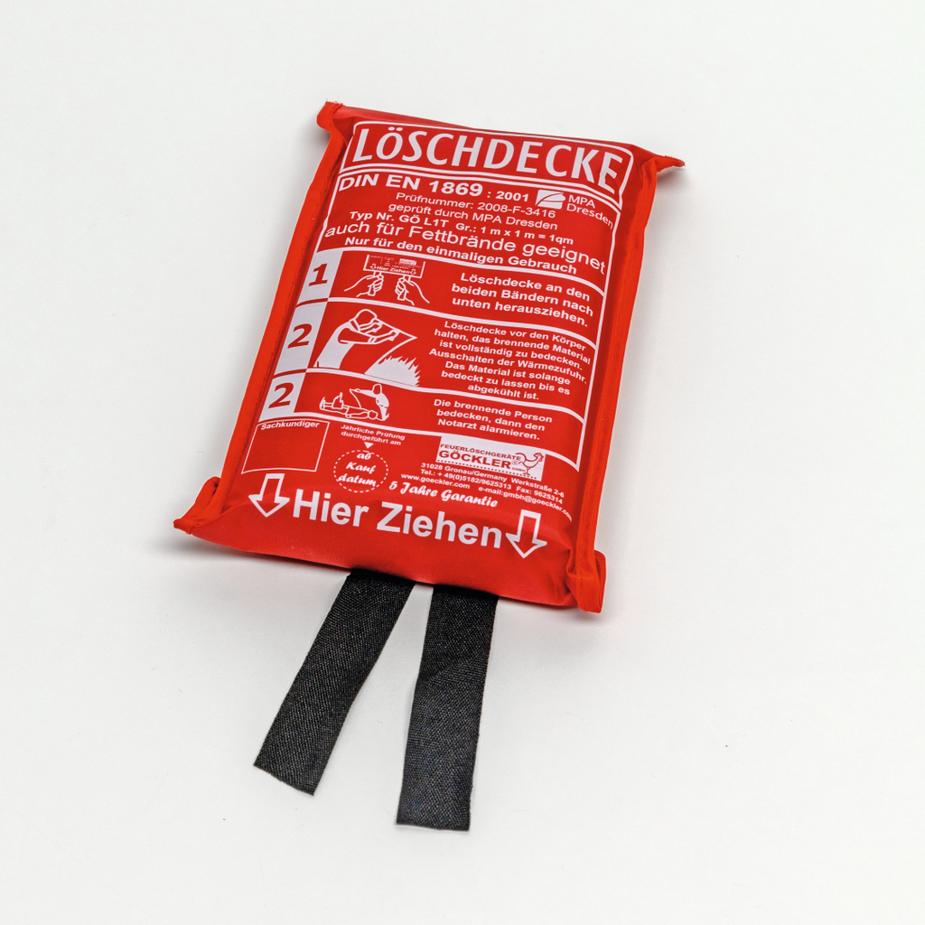 Das Bild zeigt eine Löschdecke in roter Verpackung mit Sicherheitsanweisungen. Sie ist für den einmaligen Gebrauch gedacht und dient zur Bekämpfung von Bränden, insbesondere bei brennenden Kleidung oder Gegenständen.