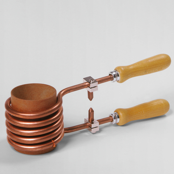 Das Bild zeigt ein metallisches Experimentiergerät mit einer spiralförmigen Kupferleitung und zwei Holzgriffen. Es wird wahrscheinlich in Schulen oder Laboreinrichtungen verwendet, um physikalische oder chemische Experimente durchzuführen.