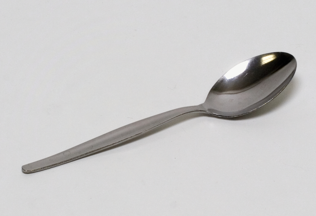 Das Bild zeigt einen einfachen, metallischen Esslöffel auf einem weißen Hintergrund. Er ist glänzend und hat eine klassische Form, die für verschiedene Experimente im Bildungsbereich verwendet werden kann.