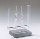 Das Bild zeigt ein Labormaterial mit mehreren Glasröhren, die auf einem grauen Standfuß befestigt sind. Die Röhren haben unterschiedliche Formen, darunter eine schlangenförmige, und scheinen für chemische Experimente oder Demonstrationen konzipiert zu sein.