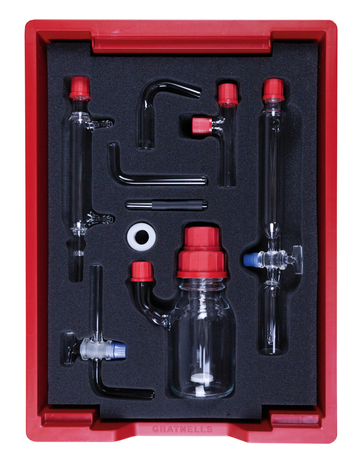 Das Bild zeigt ein Set aus Glasgeräten, das in einer roten Schaumstoffeinlage vorgesehen ist. Es umfasst verschiedene Röhren und einen Behälter mit Schraubverschluss, die für chemische Experimente im Bildungsbereich genutzt werden können.