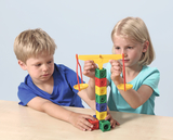 Auf dem Bild experimentieren ein Junge und ein Mädchen mit einer bunten Wippe. Sie benutzen verschiedene farbige Blöcke, um das Gleichgewicht zu testen und zu lernen, wie Gewicht und Balance funktionieren.