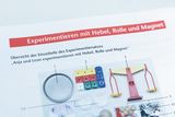 Das Bild zeigt eine Übersicht der Einzelteile eines Experimentiersatzes mit dem Thema "Hebel, Rolle und Magnet". Es sind verschiedene Materialien abgebildet, die zur Durchführung von Experimenten in der Schule verwendet werden können.