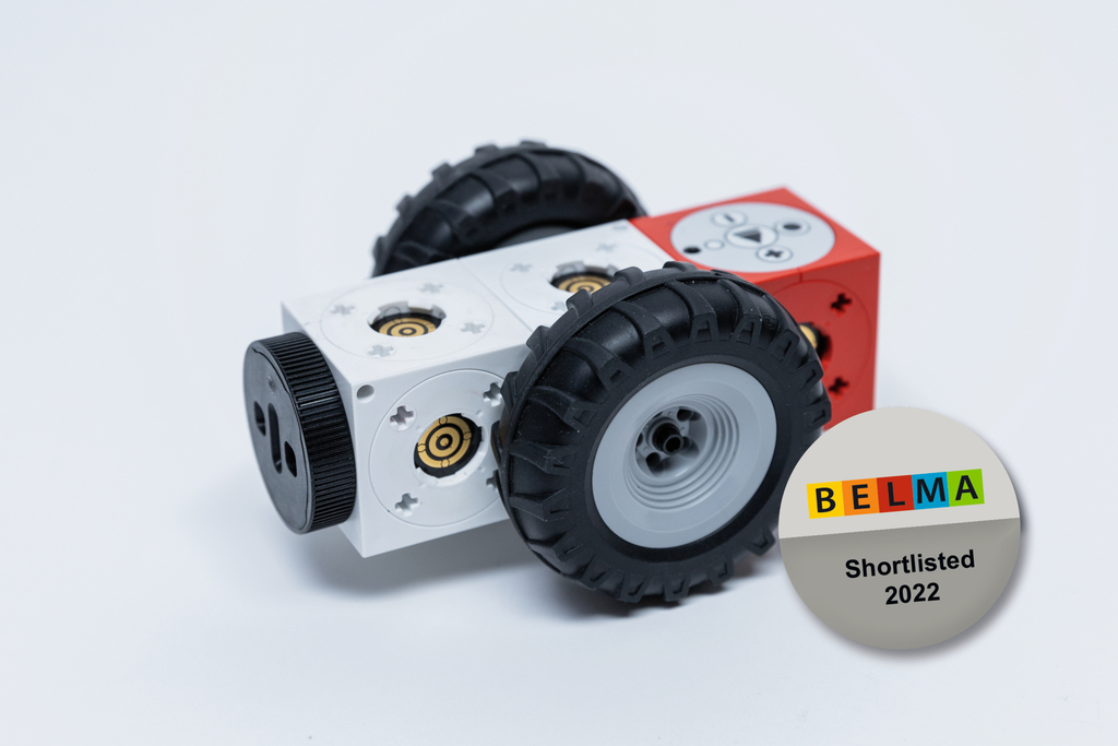 Das Bild zeigt einen kleinen, robotischen Baukasten mit Rädern in verschiedenen Farben, der für Bildungszwecke geeignet ist. Daneben befindet sich ein Auszeichnungssymbol, das darauf hinweist, dass das Produkt für den BELMA-Award 2022 nominiert wurde.