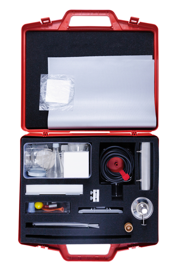 Das Bild zeigt einen roten Koffer, der eine Vielzahl von Experimentiermaterialien und -geräten enthält, darunter Messbecher, Schläuche und eine Wärmequelle. Die sorgfältige Anordnung der Utensilien deutet auf eine praktische Nutzung im Bildungsbereich hin.