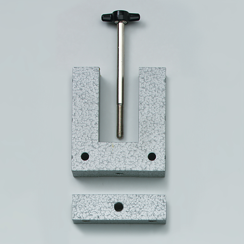 Das Bild zeigt eine graue Halterung aus Metall, die aus zwei Teilen besteht: einer U-förmigen Basis mit einer Gewindestange in der Mitte und einer flachen Platte. Diese Vorrichtung wird vermutlich für Experimentierzwecke im Bildungsbereich verwendet, um Objekte zu fixieren.