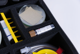 Das Bild zeigt einen Kasten mit verschiedenen Experimentiermaterialien, darunter eine Petrischale, Schnittmuster und ein Reagenzglas. Diese sind sorgfältig in einer Schaumstoffeinlage für sicheren Transport und Lagerung angeordnet.