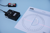 Das Bild zeigt ein Experimentiergerät mit einer Kontrollbox und einem Laserstrahl, der auf ein Messblatt mit einem Halbkreis und Skalen projiziert wird. Neben der Box befindet sich ein Batteriefach zur Stromversorgung des Geräts.