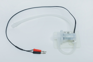 Das Bild zeigt ein Experimentiergerät mit einem transparenten Gehäuse, einem Schlauch und elektrischen Anschlüssen. Es könnte für Anwendungen in der Physik oder Chemie im Bildungsbereich verwendet werden, um unterschiedliche Aspekte des Experimentierens zu demonstrieren.