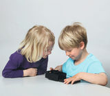 Das Bild zeigt zwei Kinder, ein Mädchen und einen Jungen, die aufmerksam auf eine schwarze Box blicken, die auf einem Tisch steht. Sie scheinen neugierig und interessiert zu sein, was sich in der Box befindet, während sie gemeinsam an dem Experimentierprojekt arbeiten.