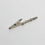 Das Bild zeigt eine silberne Krokodilklemme, die typischerweise in Experimenten und elektrischen Schaltkreisen verwendet wird. Sie hat eine praktische Befestigungsvorrichtung zur sicheren Verbindung von Drähten oder Bauteilen.