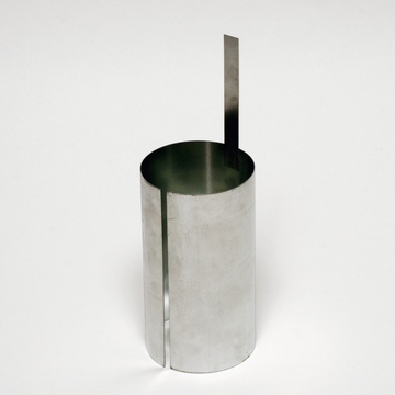 Das Bild zeigt einen zylindrischen Behälter aus Metall mit einer seitlichen Kerbe und einem vertikalen Metallstreifen, der aus dem oberen Rand herausragt. Dieses Experimentiergerät wird häufig im Bildungsbereich verwendet, um physikalische Konzepte zu demonstrieren.