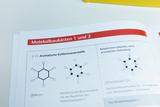 Das Bild zeigt Seiten aus einem Lehrbuch über Molekülbaukästen, die sich mit aromatischen und nicht-aromatischen Kohlenwasserstoffen befassen. Es sind Molekülstrukturen von Benzol und Cyclohexan abgebildet, mit Erklärungen zu deren Eigenschaften.