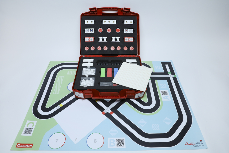 Offener Experimentierkoffer mit dem dazugeh&ouml;rigen Spielplan, auf dem die Fabrik aufgebaut werden kann. Der Spielplan ist ausgebreitet und der offene Koffer steht auf dem Spielplan. 