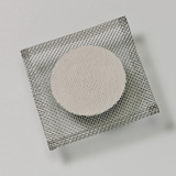 Das Bild zeigt eine runde, helle Probe, die auf einem feinmaschigen Drahtgitter platziert ist. Dieses Setup könnte für Experimente im Bildungsbereich verwendet werden, möglicherweise im Bereich der Chemie oder Materialwissenschaften.