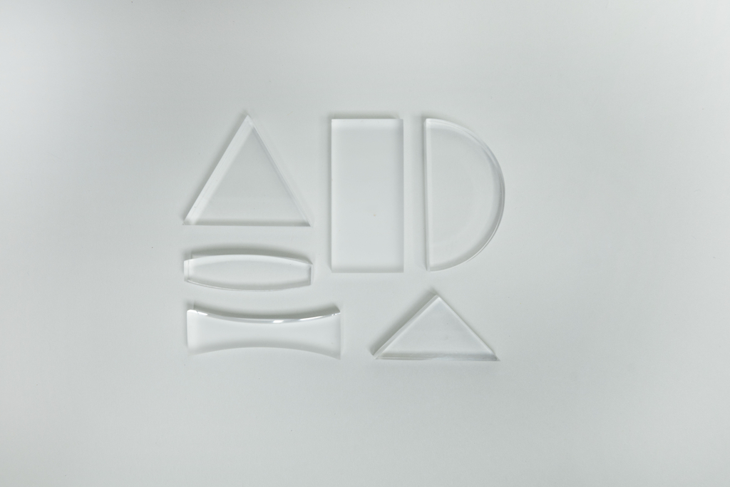 Das Bild zeigt verschiedene durchsichtige Glasteile in unterschiedlichen geometrischen Formen, darunter Dreiecke, Rechtecke und Bögen. Diese Teile dienen vermutlich als Experimentiermaterial für Bildungszwecke im naturwissenschaftlichen Unterricht.