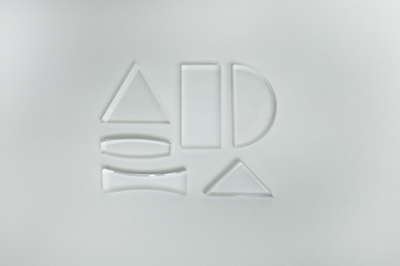 Das Bild zeigt verschiedene durchsichtige Glasteile in unterschiedlichen geometrischen Formen, darunter Dreiecke, Rechtecke und Bögen. Diese Teile dienen vermutlich als Experimentiermaterial für Bildungszwecke im naturwissenschaftlichen Unterricht.