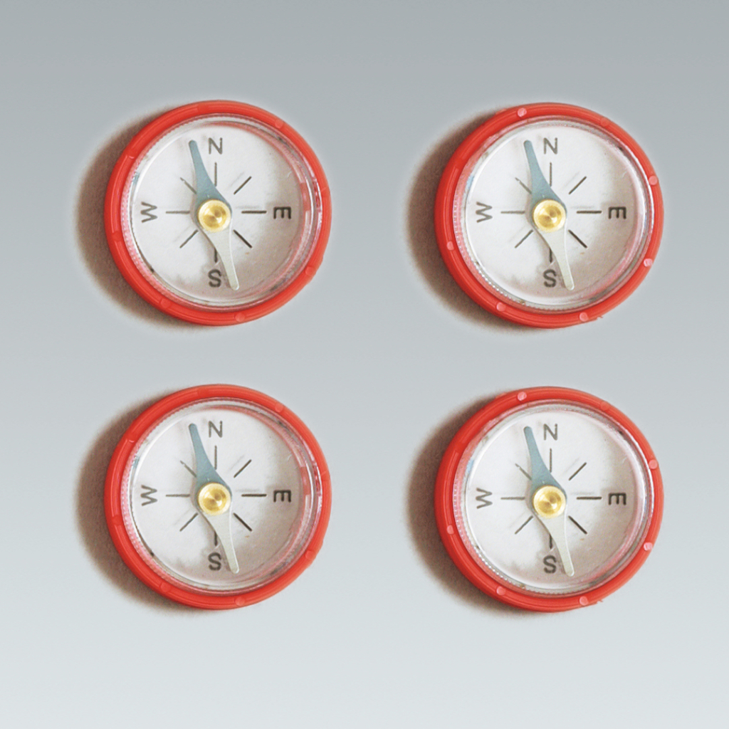Das Bild zeigt vier Kompasse in rotem Gehäuse, die gleichmäßig angeordnet sind. Jeder Kompass weist die Himmelsrichtungen Norden, Osten, Süden und Westen an, ideal für experimentelle Zwecke im Bildungsbereich.