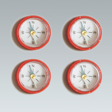 Das Bild zeigt vier Kompasse in rotem Gehäuse, die gleichmäßig angeordnet sind. Jeder Kompass weist die Himmelsrichtungen Norden, Osten, Süden und Westen an, ideal für experimentelle Zwecke im Bildungsbereich.