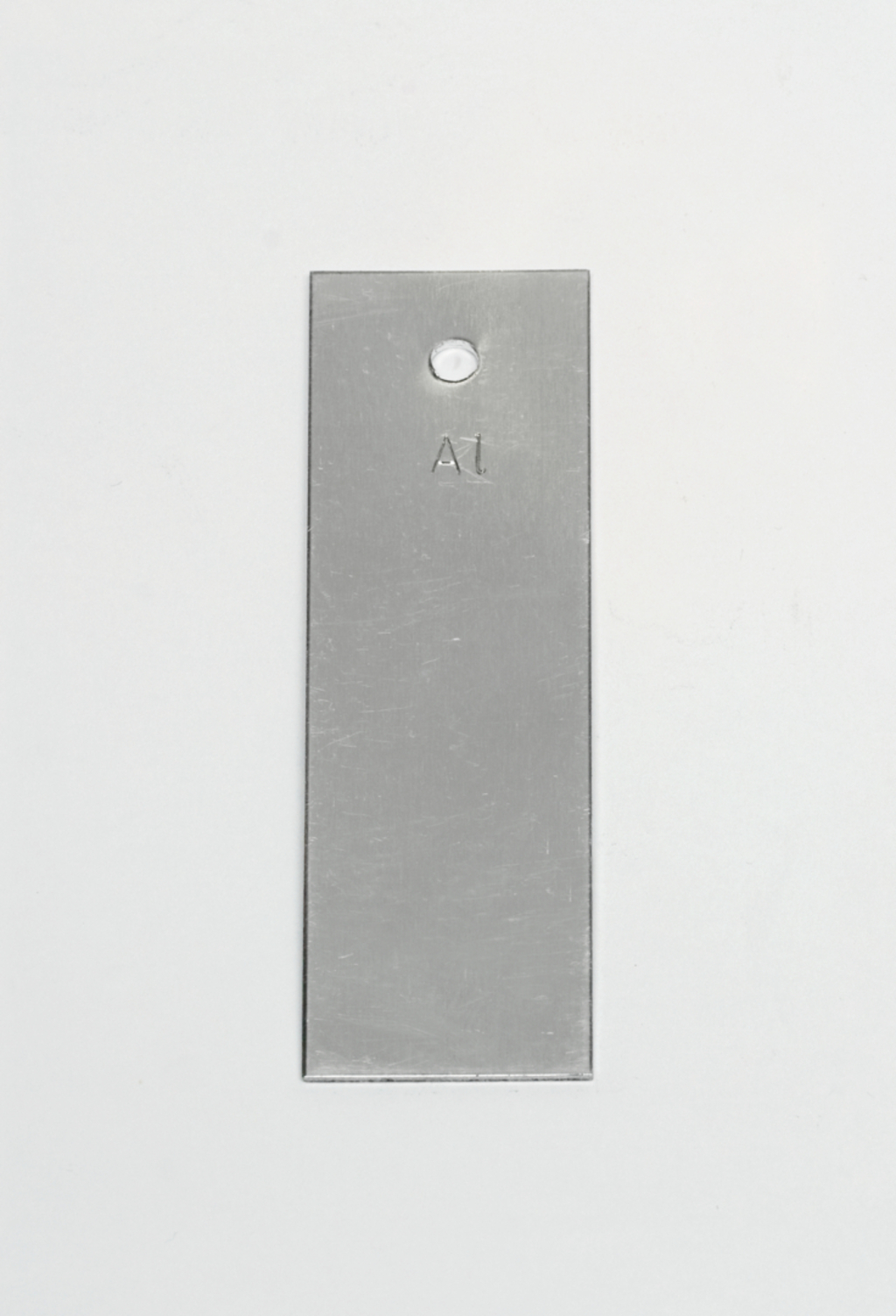 Das Bild zeigt ein rechteckiges, metallisches Objekt mit einer abgerundeten Oberkante und einem Loch in der oberen Hälfte. Auf der Vorderseite ist die Kennzeichnung „A1“ eingraviert.