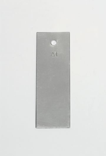 Das Bild zeigt ein rechteckiges, metallisches Objekt mit einer abgerundeten Oberkante und einem Loch in der oberen Hälfte. Auf der Vorderseite ist die Kennzeichnung „A1“ eingraviert.