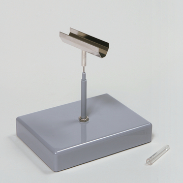 Das Bild zeigt ein Experimentiergerät, bestehend aus einer stabilen grauen Basis mit einem aufrechten Metallarm und einer schmalen Metallplatte oben. Daneben liegt ein durchsichtiges Röhrchen, das wahrscheinlich für Versuche verwendet wird.