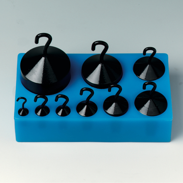 Das Bild zeigt eine Anordnung von schwarzen Hängegewichten in verschiedenen Größen, die auf einer blauen Halterung platziert sind. Diese Gewichte sind für physikalische Experimente im Bildungswesen konzipiert.