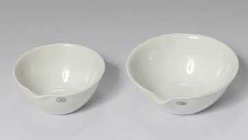 Das Bild zeigt zwei weiße, porzellanartige Küvetten in unterschiedlichen Größen. Beide Küvetten haben eine abgerundete Form und eine kleine Aussparung an der Seite, ideal für Experimente im Bildungsbereich.