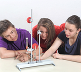 Das Bild zeigt drei Jugendliche, die gemeinsam an einem Experimentieraufbau mit einem Hebelsystem arbeiten. Sie beobachten aufmerksam, wie ein Gewicht auf einer Vorrichtung mit Rollen und einem Haken aufgestellt wird.
