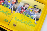 Das Bild zeigt eine gelbe Verpackung mit einer Anleitung für die "EcoLabBox", die für Experimente im Bildungswesen gedacht ist. Auf dem Cover sind cartoonartige Figuren abgebildet, die eine wissenschaftliche Untersuchung durchführen.