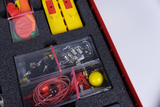 Das Bild zeigt eine Box mit Experimentiermaterialien, die für den Unterricht im deutschen Bildungswesen geeignet sind. In der Box befinden sich verschiedene Objekte wie Luftballons, kleine Elektrobauteile und metallische Komponenten, die für verschiedene Experimente genutzt werden können.