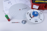 Das Bild zeigt verschiedene wissenschaftliche Experimentiermaterialien, darunter eine runde Messskala und eine Zielscheibe mit radialen Linien. Zusätzlich sind mehrere magnetische Komponenten und eine Anleitung zur Durchführung von physikalischen Experimenten abgebildet.