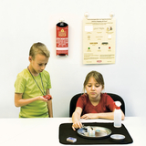 Das Bild zeigt zwei Kinder, die an einem Experimentierprojekt arbeiten. Der Junge hält eine rote Sicherheitsdecke in der Hand, während das Mädchen mit einem Behälter auf einem Tablett arbeitet, um ein Experiment durchzuführen.