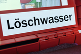 Das Bild zeigt eine rote Box mit dem klaren Aufdruck „Löschwasser“. In der Box sind verschiedene Materialien sichtbar, die für experimentelle Zwecke im Bildungsbereich verwendet werden, einschließlich chemischer Reagenzien und weiterer Ausstattungen.