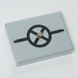 Das Bild zeigt ein elektrisches Experimentiergerät in grauer Farbe mit einer zentralen Glühbirne und einem stilisierten Schaltkreis-Design auf der Oberseite. Es ist für Bildungszwecke konzipiert und dient vermutlich zur Demonstration von elektrischen Schaltungen.