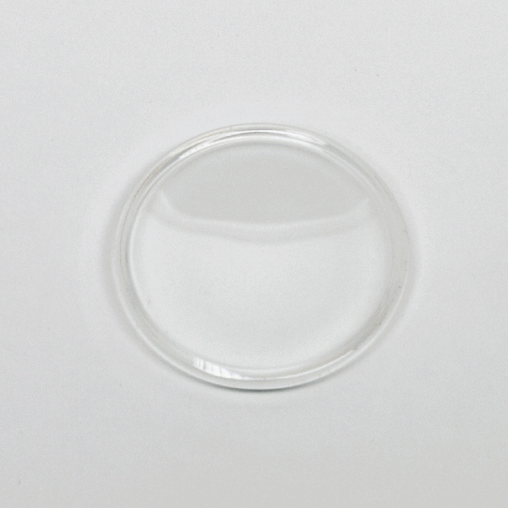 Das Bild zeigt eine klare, runde Glasplatte, die wahrscheinlich als Objektträger für mikroskopische Untersuchungen verwendet wird. Der Hintergrund ist hell und neutral, was den Fokus auf das Glasobjekt lenkt.