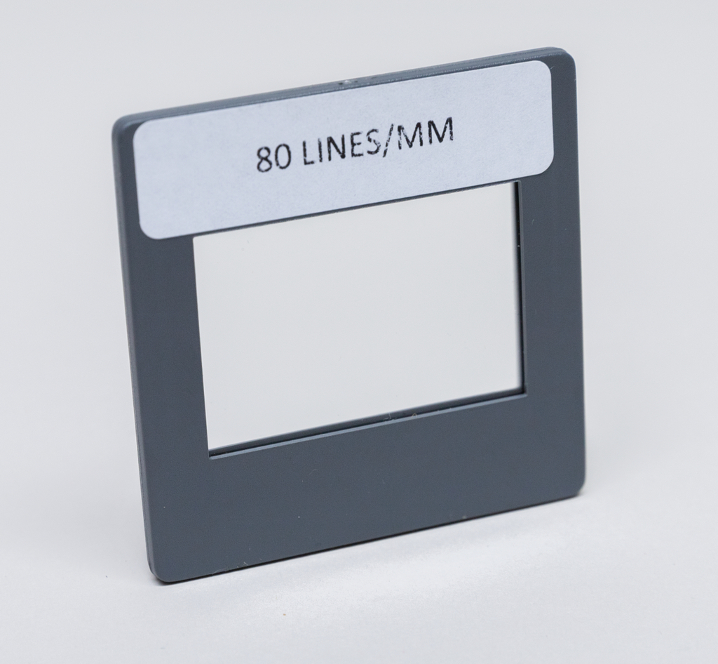 Das Bild zeigt einen rechteckigen Rahmen mit einer Öffnung in der Mitte. Auf dem Rahmen ist die Aufschrift „80 LINES/MM“ zu sehen, was auf seine Verwendung für optische Experimente hindeutet.