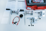 Das Bild zeigt ein Experimentierkit, das verschiedene Komponenten wie Motor, Klemmen, Kabel und eine Anleitung für Lernexperimente umfasst. Es dient zur praktischen Durchführung von Versuchen im Bereich der physikalischen Bildung.