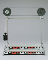 Das Bild zeigt ein physikalisches Experimentiergerät mit einem Pulley-System. An einem Seil hängt ein Gewicht, welches zur Demonstration von Kräften und Bewegung verwendet werden kann.
