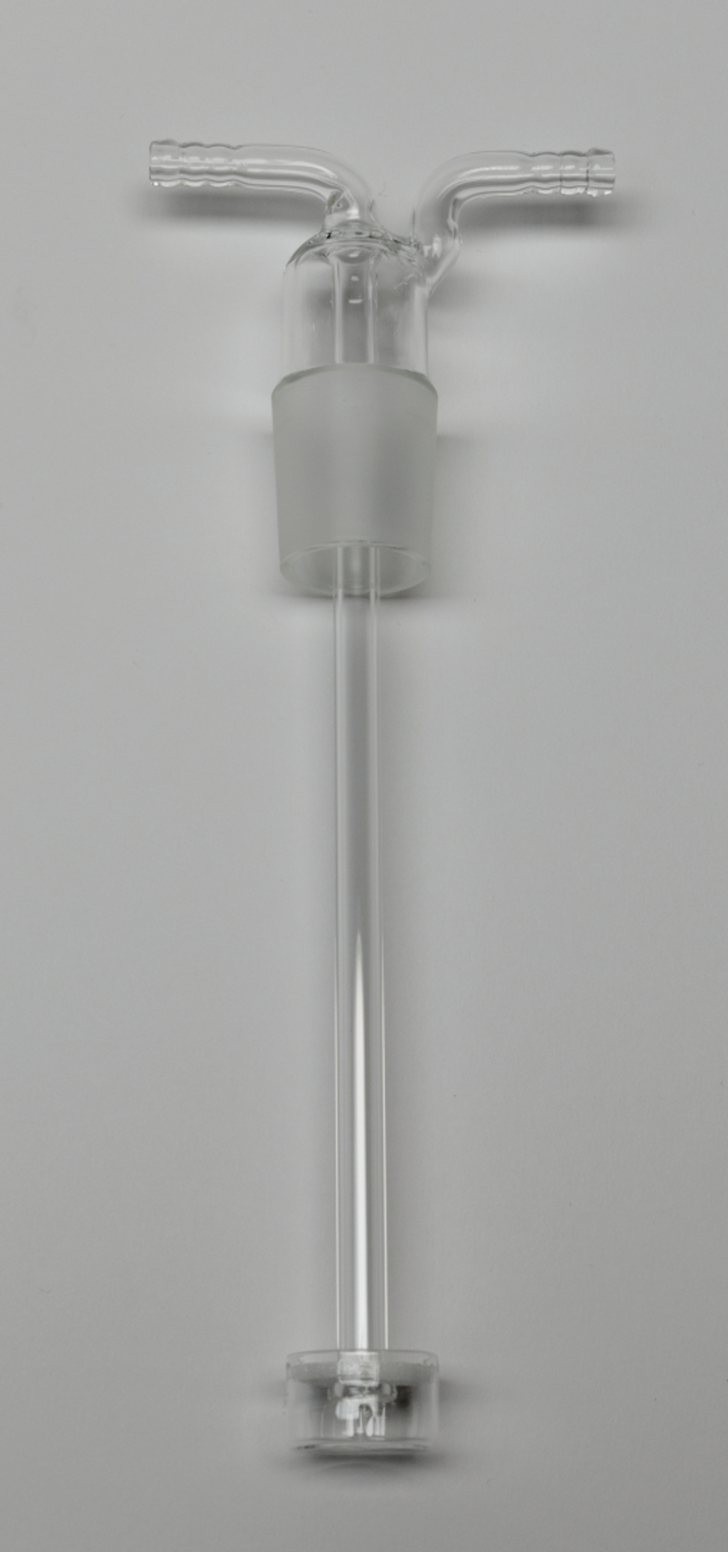 Das Bild zeigt ein transparentes Glasgerät, vermutlich eine Apparatur für chemische Experimente. Es besitzt einen langen Schlauch mit zwei seitlichen Abgängen, ideal für das Anbringen an eine andere Vorrichtung oder für das Durchführen von Experimenten.
