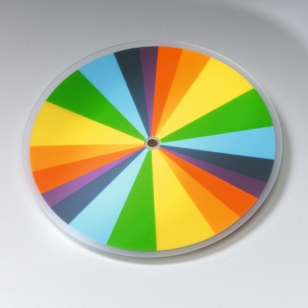 Das Bild zeigt einen farbenfrohen Kreisel mit einem kreisrunden Design, das in verschiedene segmentierte Farbbereiche unterteilt ist. Diese lebendigen Farben können für Experimente zur Farbtheorie oder zur Demonstration von Lichtstreuung genutzt werden.