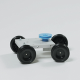 Das Bild zeigt ein einfaches Modellfahrzeug mit einem weißen Fahrgestell und vier schwarzen Rädern. In der Mitte befindet sich eine hellblaue Drehscheibe, die möglicherweise für experimentelle Zwecke genutzt werden kann.