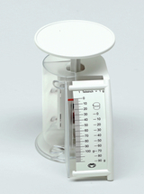 Das Bild zeigt eine transparente Waage mit einer runden Plattform und einer seitlichen Skala. Die Skala ist in Gramm unterteilt und reicht von 0 bis 90 g, um genaue Messungen für Experimente zu ermöglichen.