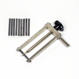 Das Bild zeigt ein Experimentiergerät aus Metall, das aus einem Rahmen mit einer verstellbaren Plattform besteht. Daneben liegen mehrere metallene Stäbe, die vermutlich als Zubehör für verschiedene Experimente dienen.