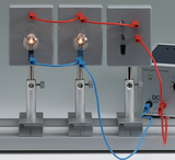 Das Bild zeigt ein Experimentiergerät mit zwei Glühbirnen, die durch farbige Kabel verbunden sind. Neben den Birnen befindet sich ein Gleichstromnetzgerät, das für elektrische Experimente im Bildungsbereich verwendet wird.
