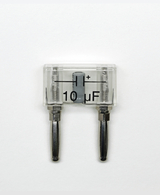 Das Bild zeigt einen Kondensator mit einer Kapazität von 10 μF, der in einem transparenten Gehäuse untergebracht ist. Die beiden Anschlussleitungen sind deutlich erkennbar und der Kondensator ist positiv markiert.