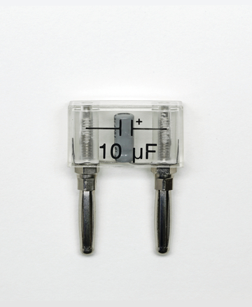 Das Bild zeigt einen Kondensator mit einer Kapazität von 10 μF, der in einem transparenten Gehäuse untergebracht ist. Die beiden Anschlussleitungen sind deutlich erkennbar und der Kondensator ist positiv markiert.