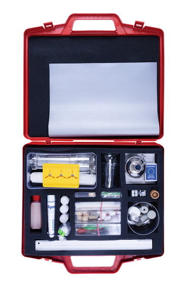 Das Bild zeigt einen roten Koffer, der mit verschiedenen Experimentiermaterialien ausgestattet ist, darunter Glasbehälter, Chemikalien, Messgeräte und Zubehör. Diese Materialien sind übersichtlich angeordnet und eignen sich für den Einsatz im Bildungsbereich.